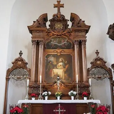 Geschmückter Holzaltar mit Blumen, Kerzen und dem Altarbild, das Jesus mit den Emmausjüngern zeigt.